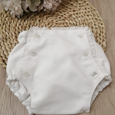 Fralda branca para bebé com botões transparentes e borda de renda sobre suporte de palha