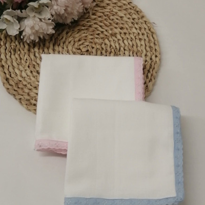 Dois panos brancos com bordas rendadas azul e rosa em base trançada bege com flores artificiais.