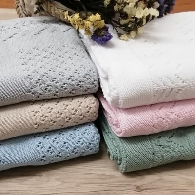 Seis mantas ou toalhas de malha em várias cores empilhadas numa mesa de madeira