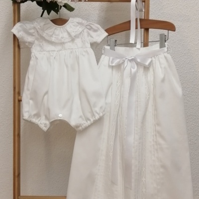 Conjunto de roupa de bebé branco com macacão e calça comprida pendurado em estrutura de madeira