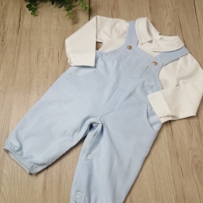 Conjunto de jardineiras azuis claras com camisa branca para bebé sobre superfície de madeira