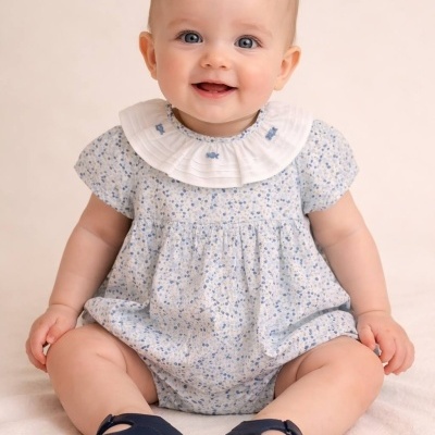 Bebé com vestido azul claro e sapatos azuis escuros sentado num fundo bege