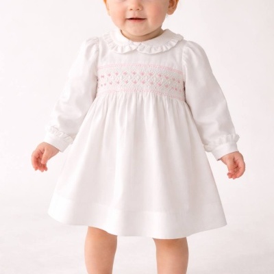 Bebé de vestido branco com bordados rosas e sapatinhos brancos