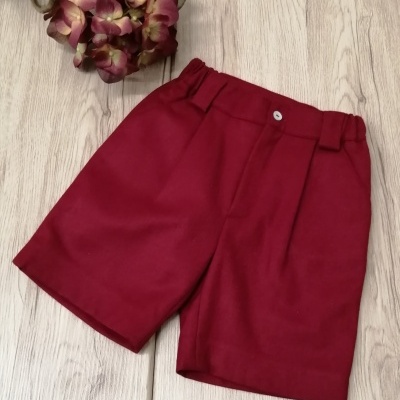 Calções vermelhos com cós elástico e botão branco ao lado de flor artificial