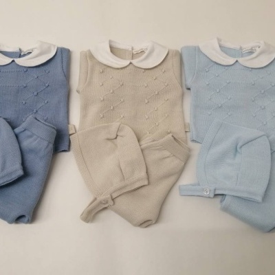 Três conjuntos de roupa de bebé em azul royal, bege e azul claro com camisolas de malha, calças e gorros.