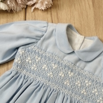 Vestido infantil azul claro com bordado de flores brancas e flores ao fundo