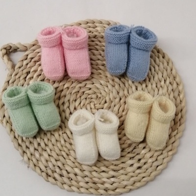 Cinco pares de meias infantis tricotadas multicoloridas sobre tapete redondo de fibras naturais.