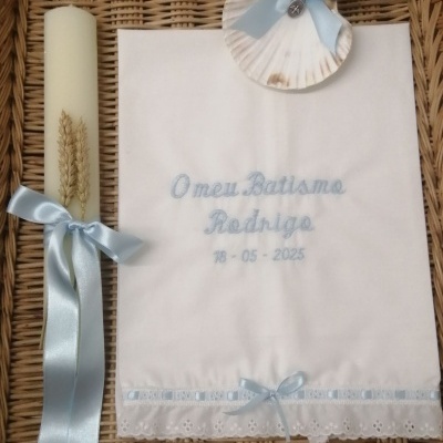 Vela e toalha de batismo branca com detalhes em azul claro sobre vime trançado