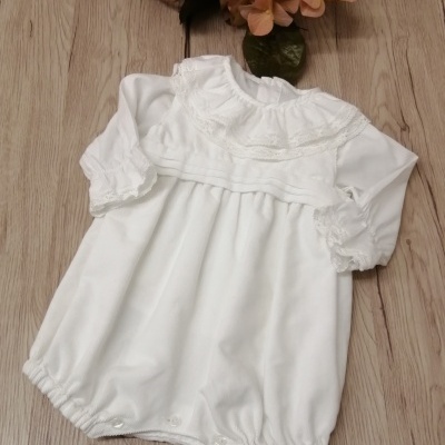 Macacão branco para bebé com renda e botões sobre madeira clara com flores