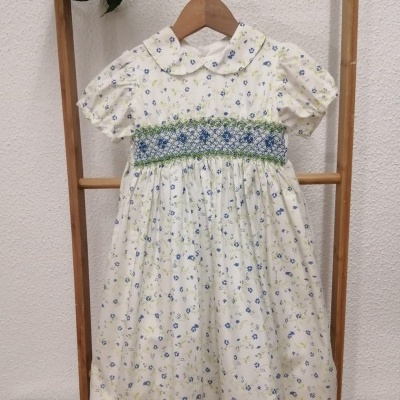 Vestido infantil branco com flores azuis e verdes e faixa bordada azul e verde.