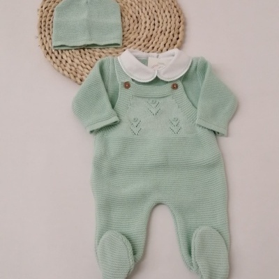Conjunto de roupa de bebé verde-água com macacão tricotado e gorro, sobre base redonda de fibras naturais