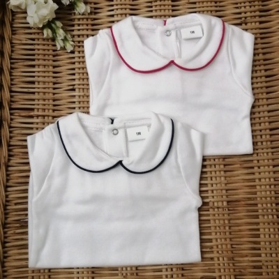 dois bodies brancos para bebé com gola contrastante rosa e azul sobre base de vime