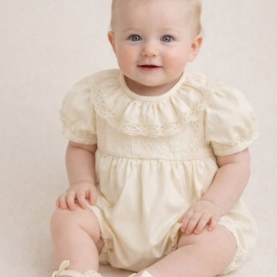 Bebé com macacão creme rendado e sapatos pérola sentada