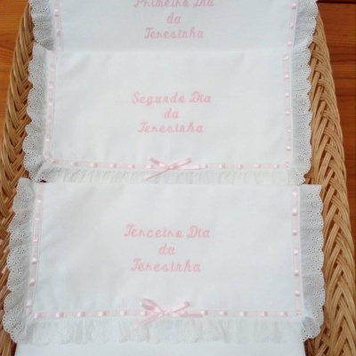 Paninhos brancos bordados com inscrições em rosa dentro de cesta de vime