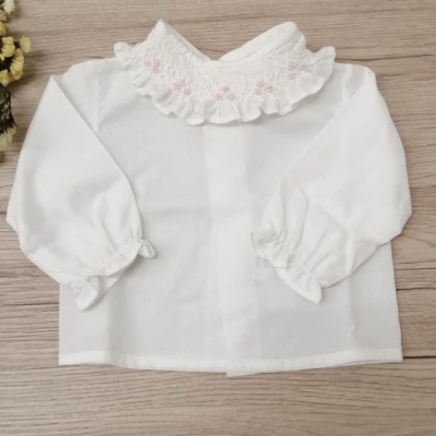 Camisa branca de bebé com gola bordada e manga longa sobre madeira