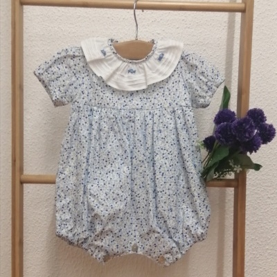 Body de bebé floral azul e branco com gola pregueada, pendurado numa estrutura de madeira