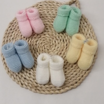 Cinco pares de botins de bebé coloridos sobre suporte redondo trançado.