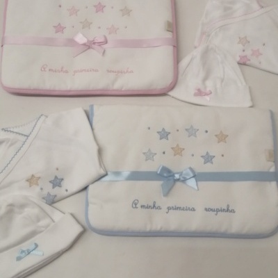 Conjunto de roupas e acessórios para bebé com estrelas bordadas e laços rosa e azul.