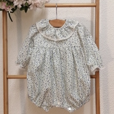 Macacão de bebé creme com flores, gola franzida e mangas compridas pendurado num cabide de madeira