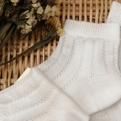 Par de meias brancas com padrões de malha sobre superfície de vime e flores secas