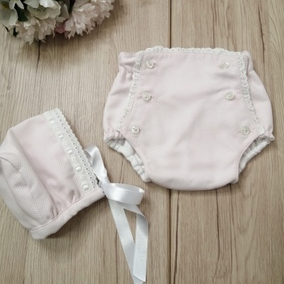 Conjunto de bebé rosa claro com botões, renda e fita de cetim sobre madeira clara