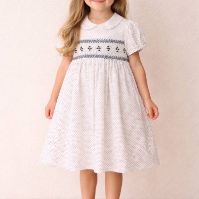 Menina com vestido branco com pontos pretos e bordado azul e sapatos azuis escuros