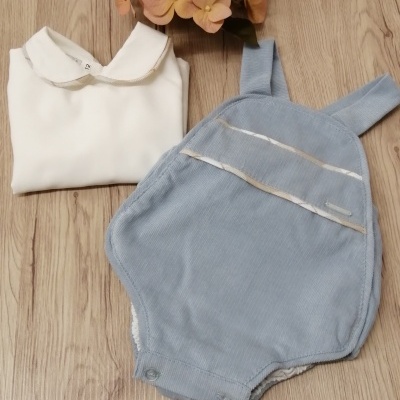 Conjunto de roupa de bebé branca e azul claro sobre superfície de madeira com flores.