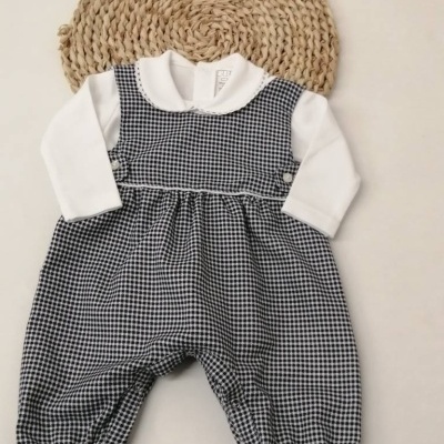 Macacão de bebé em padrão aos quadrados preto e branco com camisa branca e gola arredondada, sobre tapete redondo trançado