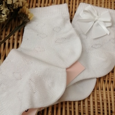 Meias brancas tricotadas com laço branco sobre superfície de vime com flores secas amarelas ao lado