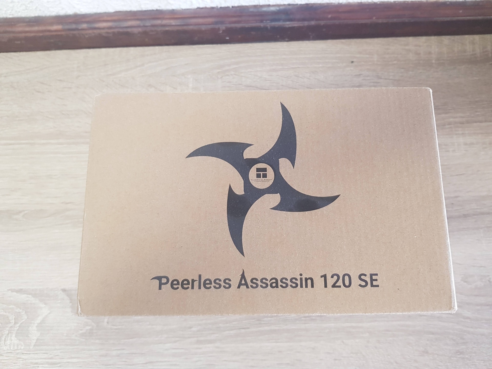 Peerless Assassin 120 SE CPU COOLER Caixa de papelão marrom com texto Peerless Assassin 120 SE e logótipo preto