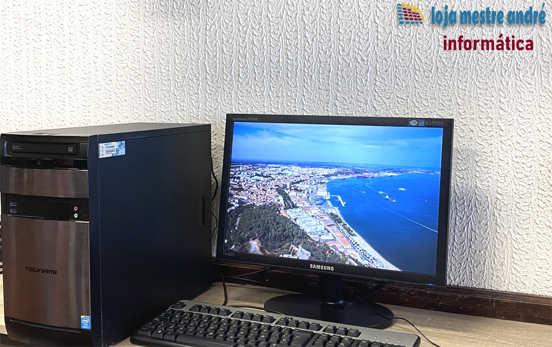 TSUNAMI Computador desktop com torre Tsunami e monitor Samsung a mostrar imagem aérea de cidade e mar