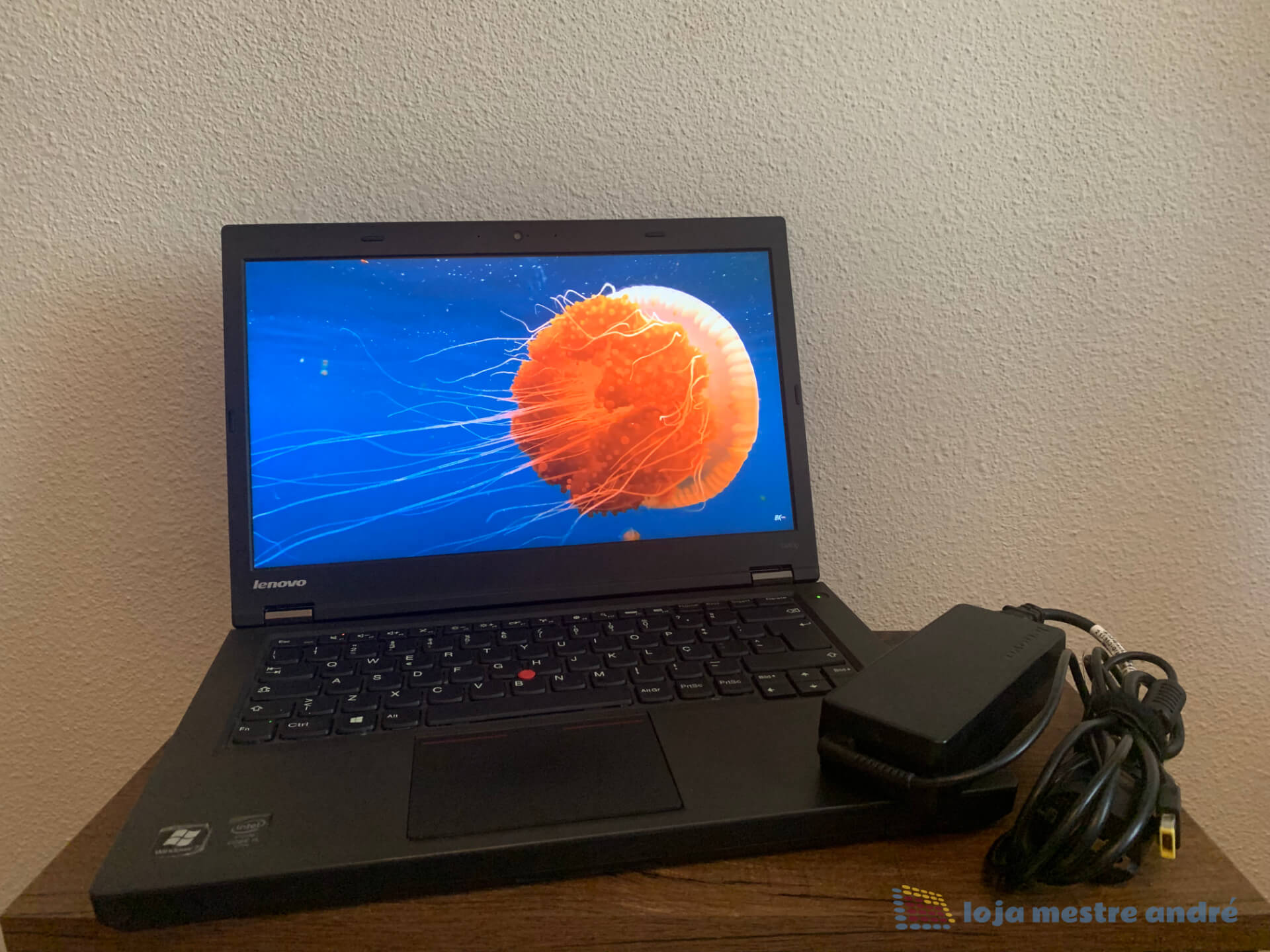 Computador portátil Lenovo ThinkPad T440p Intel Core i5 SSD 240GB RAM 8GB Windows 11 PRO Portátil Lenovo preto com imagem de água-viva laranja no ecrã e carregador ao lado sobre madeira.