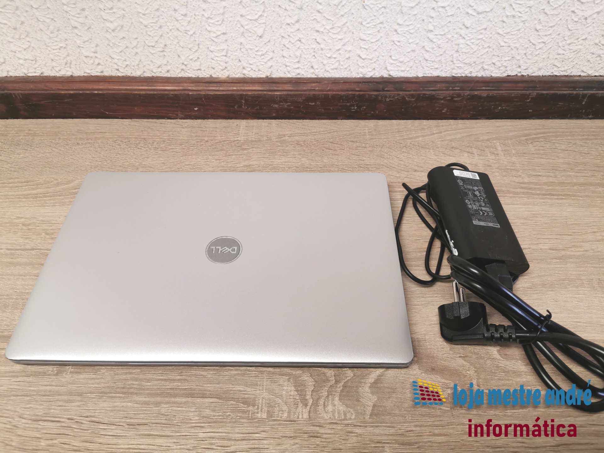 DELL Latitude 5310 Computador portátil cinza prateado Dell com carregador preto sobre mesa de madeira sobre fundo branco texturado