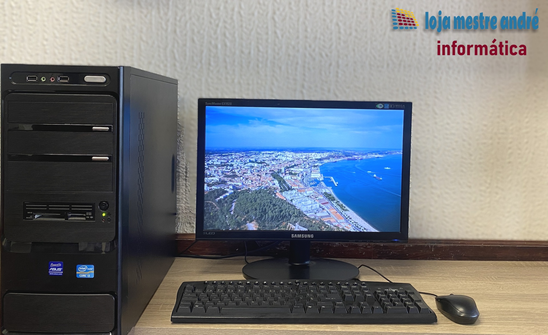 LMA B2 Computador de secretária preto com teclado, rato e monitor Samsung LED a mostrar imagem aérea do litoral.