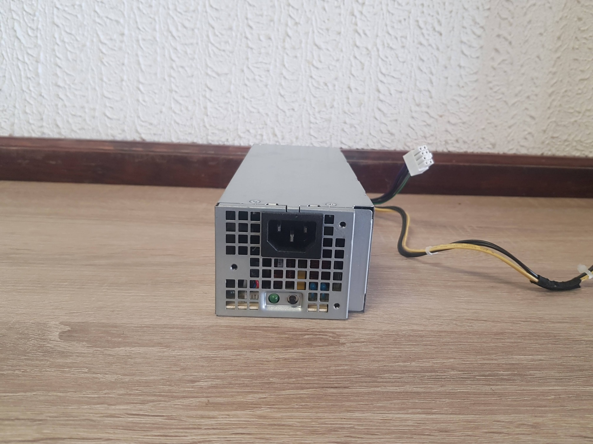 Fonte de Alimentação DELL 240w Fonte de alimentação para computador metálica prateada com cabos e conectores sobre chão de madeira clara