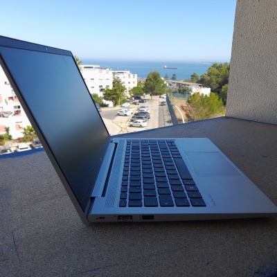 Computador portátil prateado semi-aberto sobre superfície em betão com vista para o mar