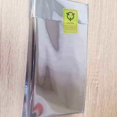 Embalagem metálica prateada com etiqueta amarela de aviso, sobre superfície de madeira clara.