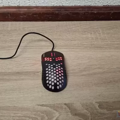 Rato de computador preto com design perfurado colocado sobre chão de madeira clara