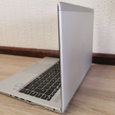 Computador portátil prateado aberto em piso de madeira com parede branca texturizada