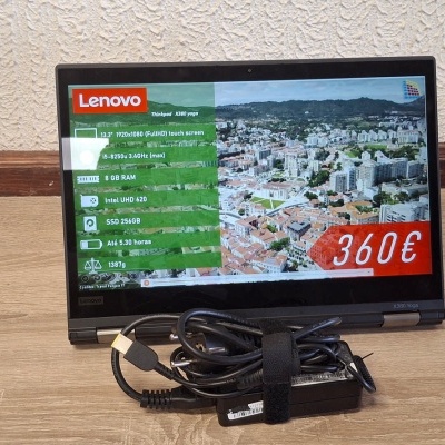 Monitor portátil Lenovo preto com ecrã a mostrar informações e preço de 360€, adaptador e cabos no chão de madeira