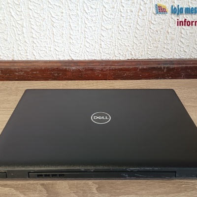 Portátil preto Dell fechado numa mesa de madeira com parede branca ao fundo.