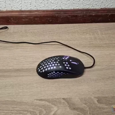 Rato de computador preto com iluminação roxa em padrão de buracos sobre chão de madeira clara