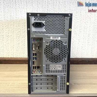 Computador de secretária preto e cinza visto de trás com portas e ventoinha, sobre mesa de madeira clara e parede texturizada de fundo.