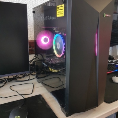 Computador desktop preto com vidro temperado e ventoinhas RGB numa secretária com rato e monitor