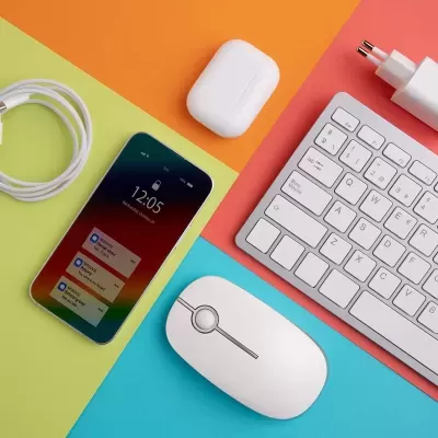 Smartphone, auscultadores, rato, teclado e carregador brancos sobre fundo colorido