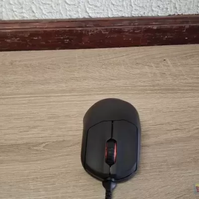 Rato de computador preto com scroll vermelho numa mesa de madeira clara