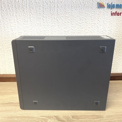 torre de computador preta sobre chão de madeira junto a parede branca com logótipo de loja de informática
