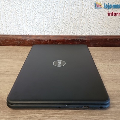 Portátil Dell preto fechado numa mesa de madeira com parede branca ao fundo