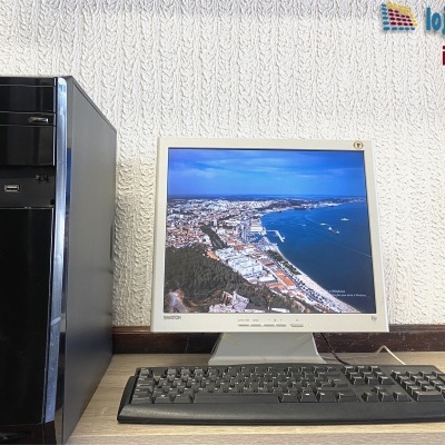 Computador de secretária com monitor, teclado e rato contra parede branca texturada