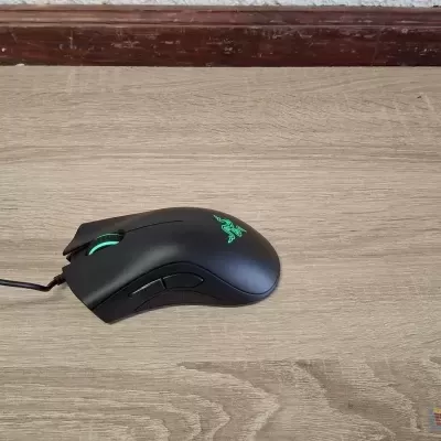 Rato de computador preto com luz verde sobre superfície de madeira clara